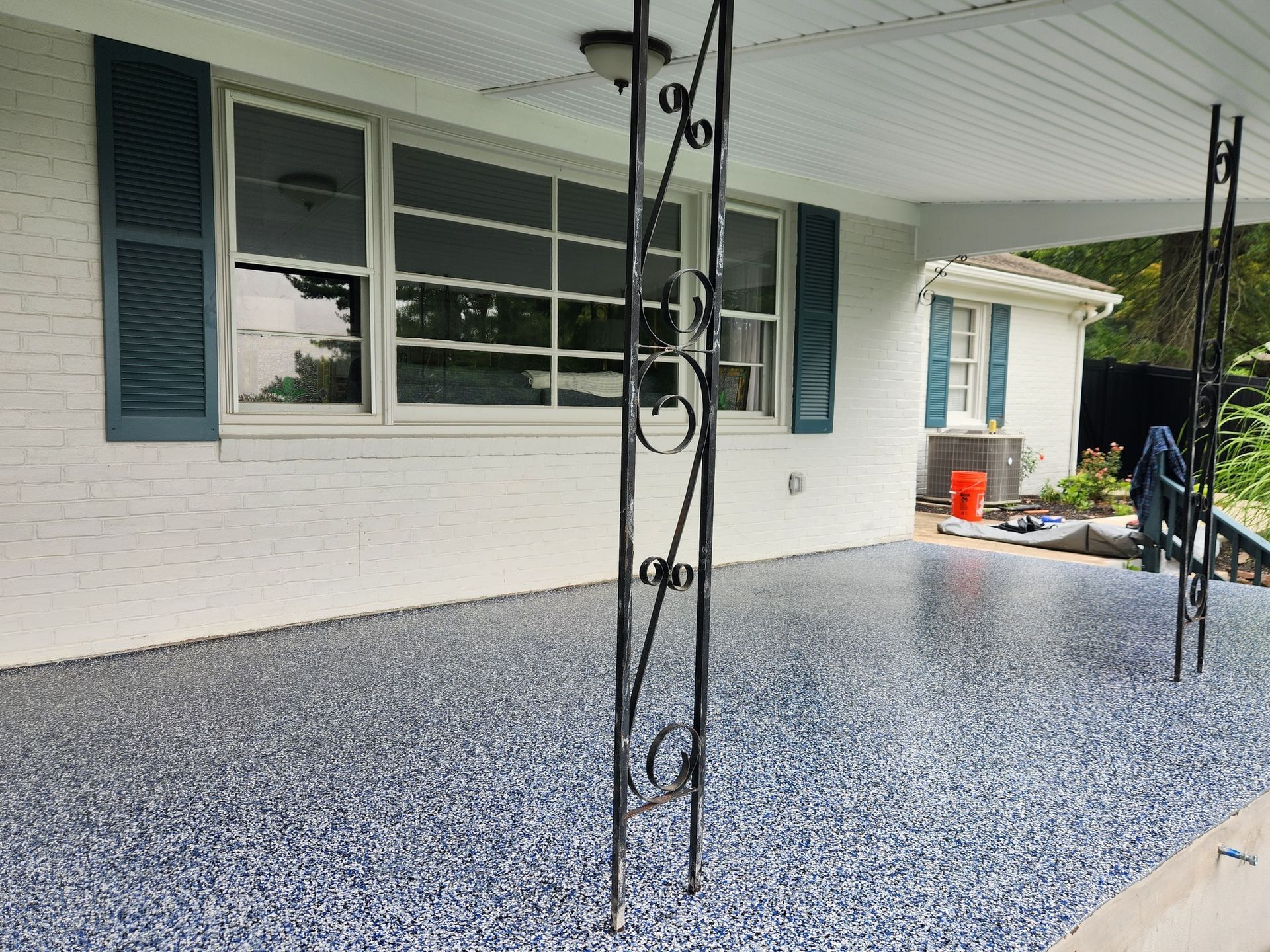 Blue speckled epoxy porch floor with white brick wall, windows, and teal shutters.