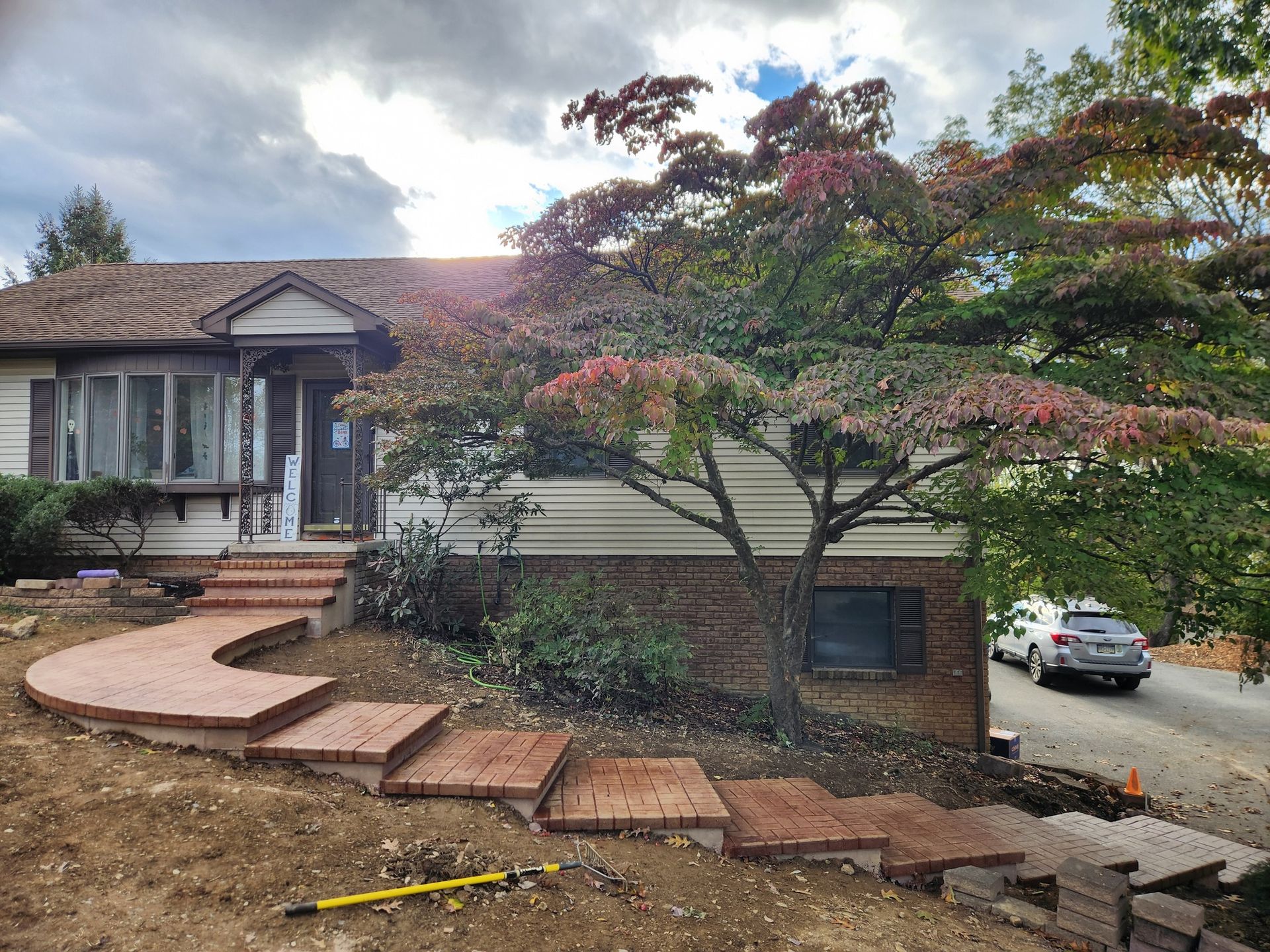Brown brick steps lead to a house with beige siding and a large tree in front.