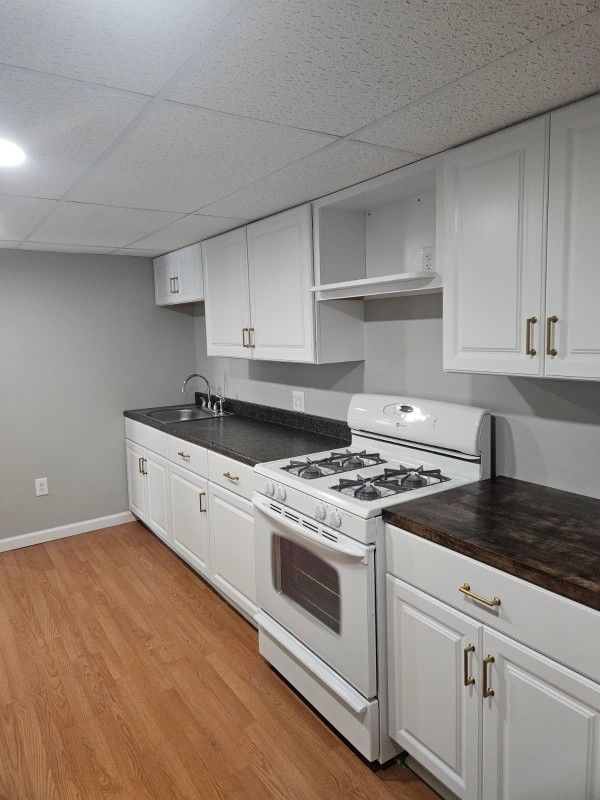 White kitchen cabinets and appliances with dark countertops, wood floors, and gray walls.