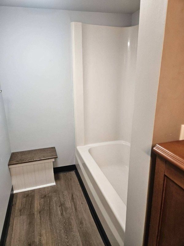 Bathroom with a white tub/shower unit, a wooden bench, and wood-look flooring.