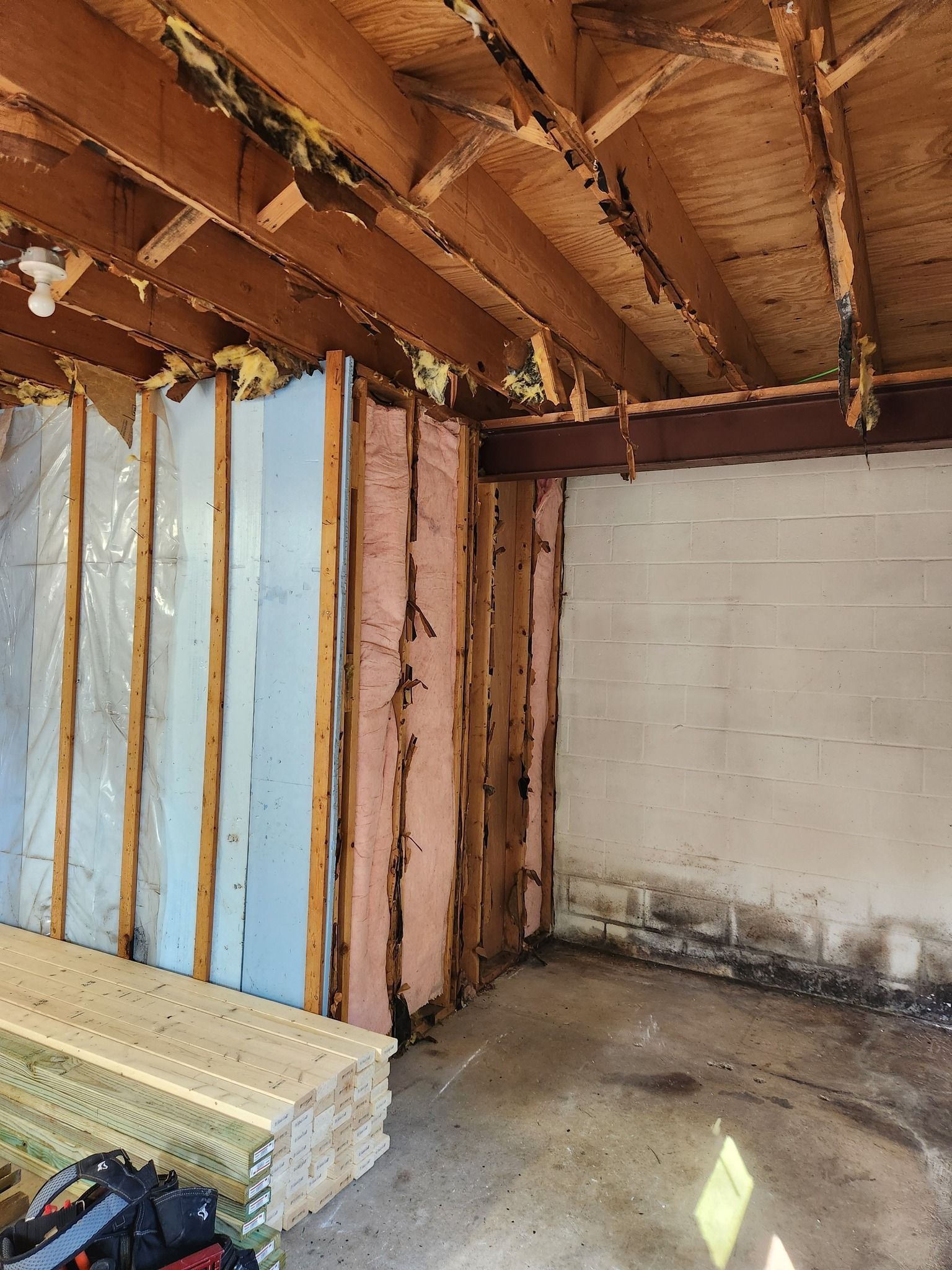 Basement interior under construction: exposed framing, insulation, concrete walls, and ceiling with exposed beams.