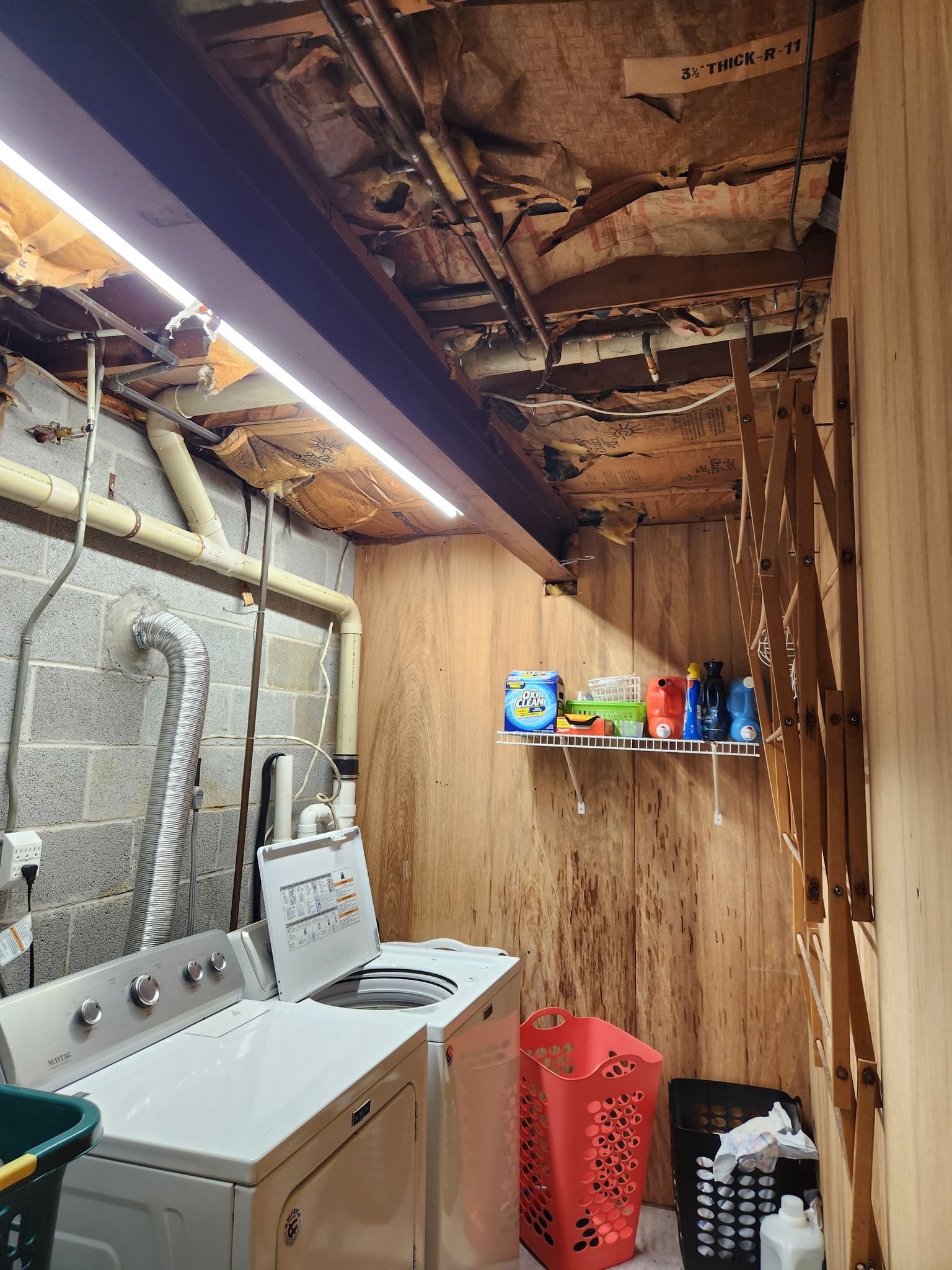 Laundry room with washer, dryer, laundry supplies on a shelf, and wooden walls.