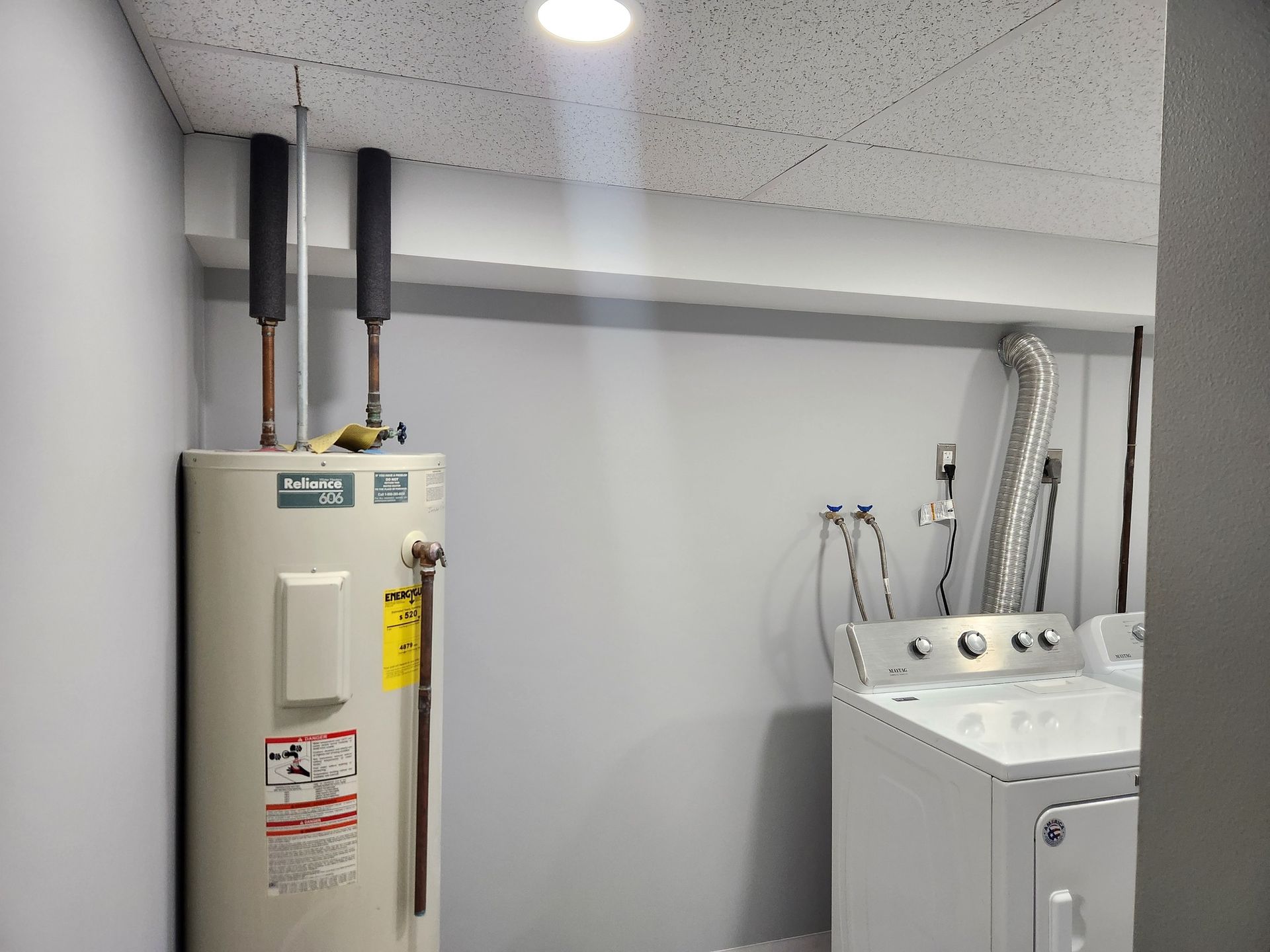 Water heater and washing machine in a gray laundry room with insulated pipes.