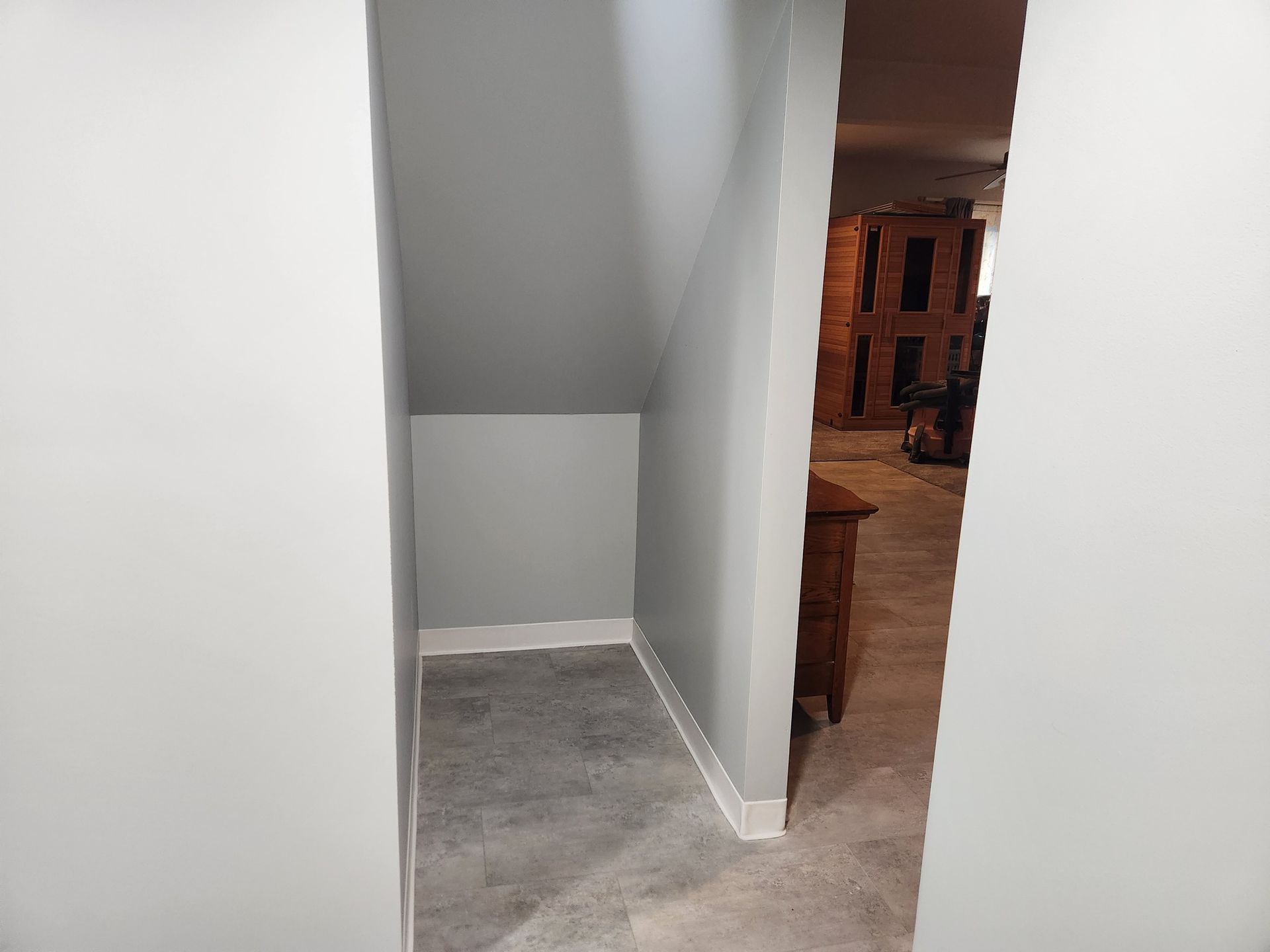 Empty closet nook with gray walls and carpet, leading to a room with furniture.