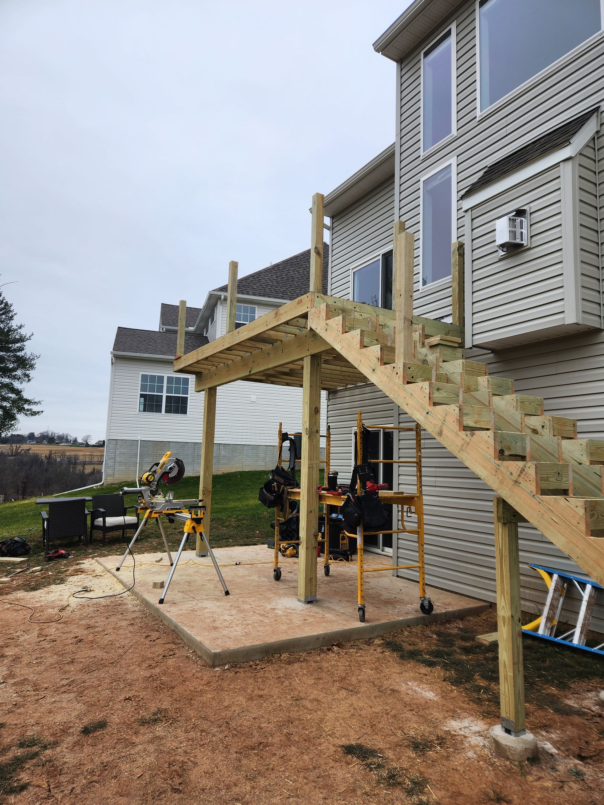 A partially constructed wooden deck with stairs extending from a house onto a gravel area with construction equipment.