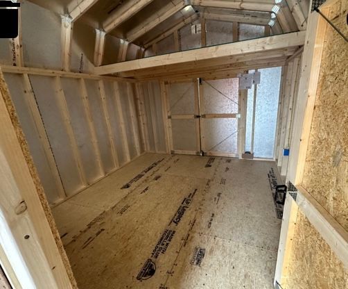 Interior view of an unfinished shed with wooden frame, open floor, and high ceiling with beams.