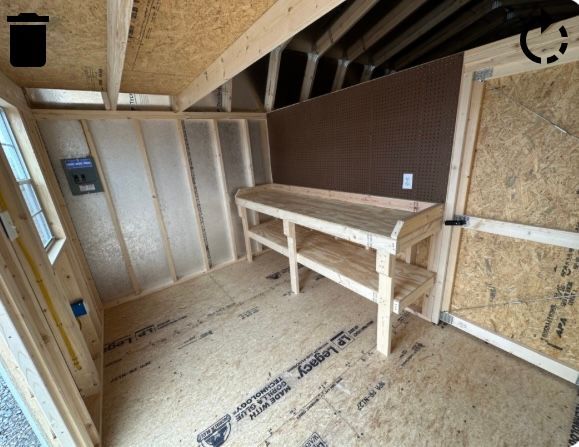 Inside a wooden shed, a workbench sits against the back wall with a pegboard.