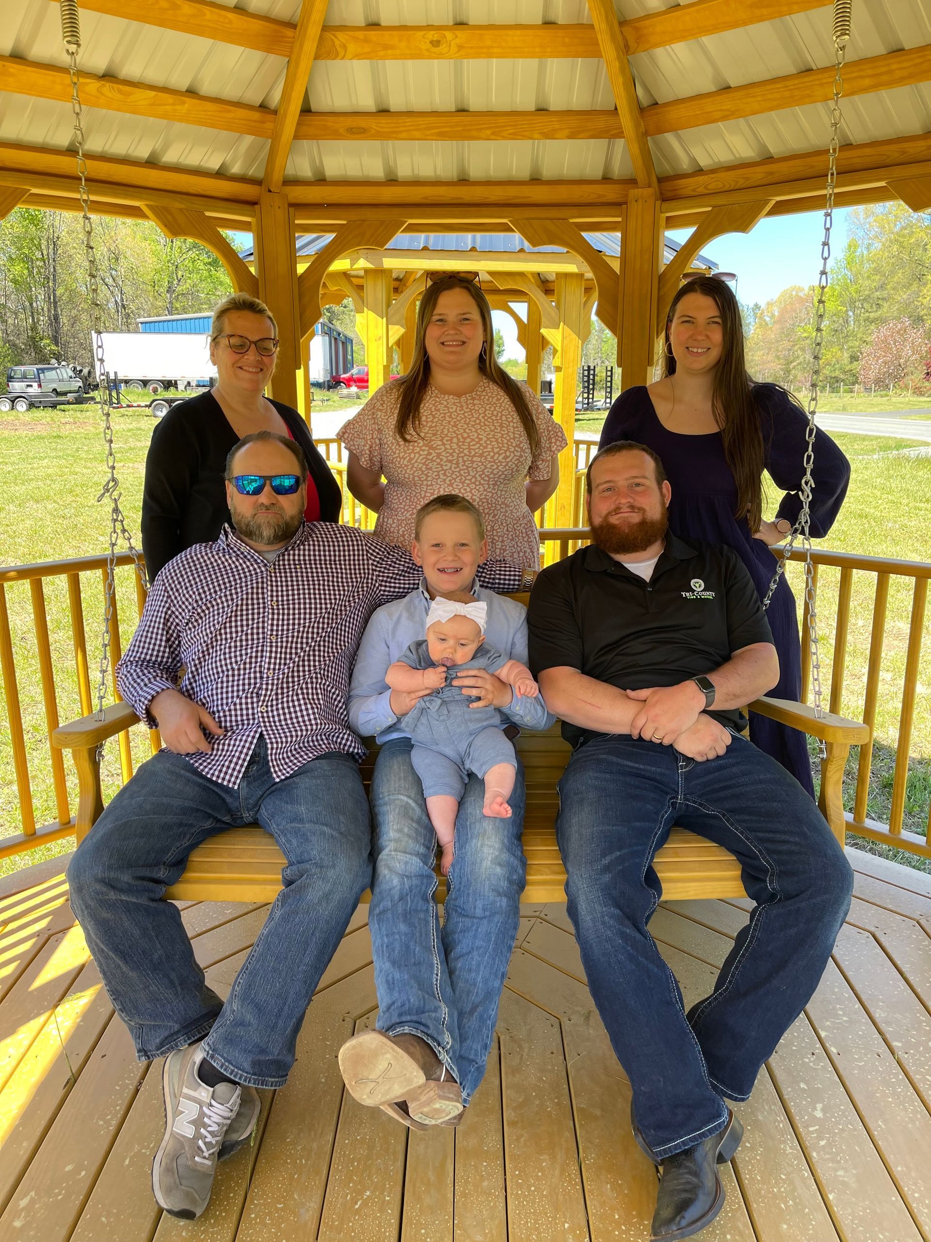 Group of seven people posing inside a yellow gazebo.  A baby is held by a person sitting between two men