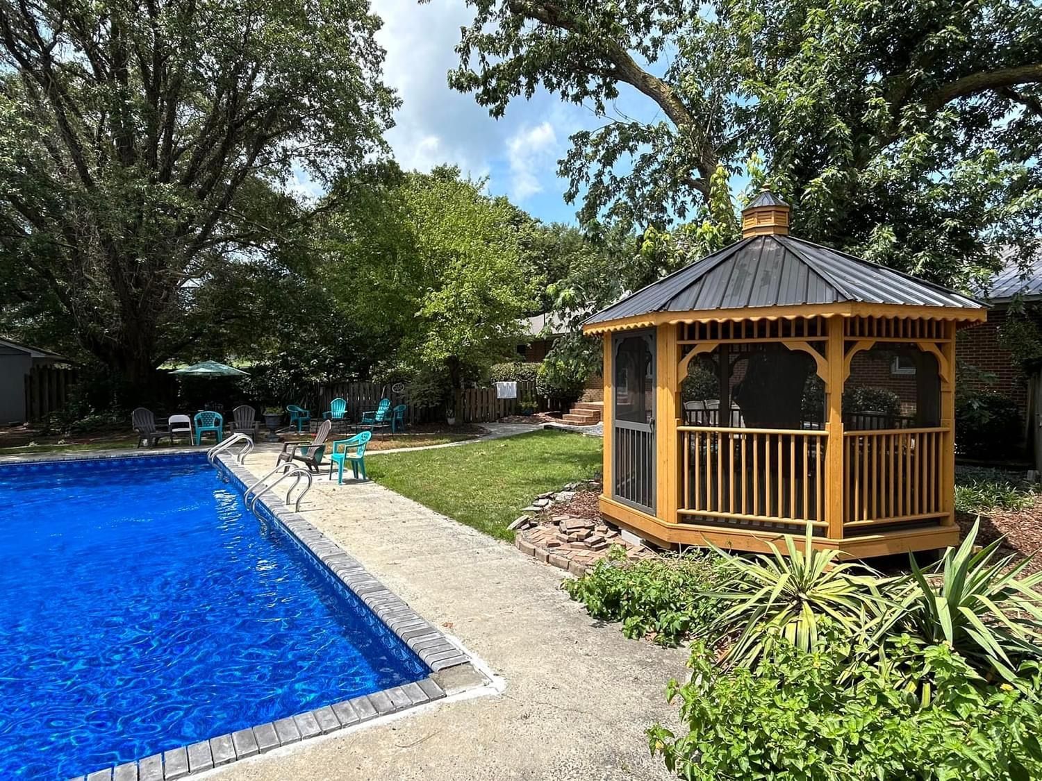 A backyard with a pool and a wooden gazebo. The pool has bright blue water.