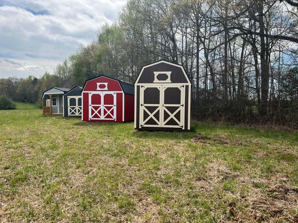 Three colorful sheds of varying sizes stand in a grassy field, with a forest in the background.
