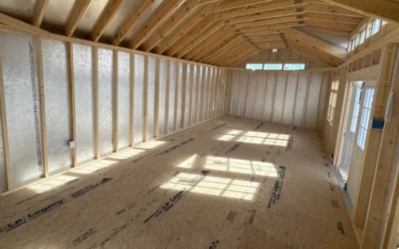Interior view of a wooden framed structure with natural lighting. Walls and ceiling are bare, with insulation visible.