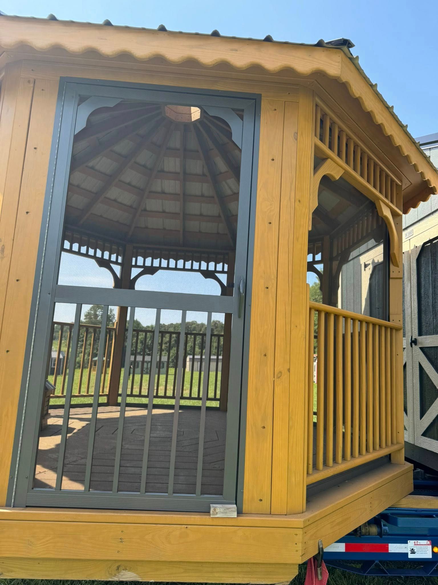 Wooden gazebo with open front door, a railing on the side, and a partially visible roof.