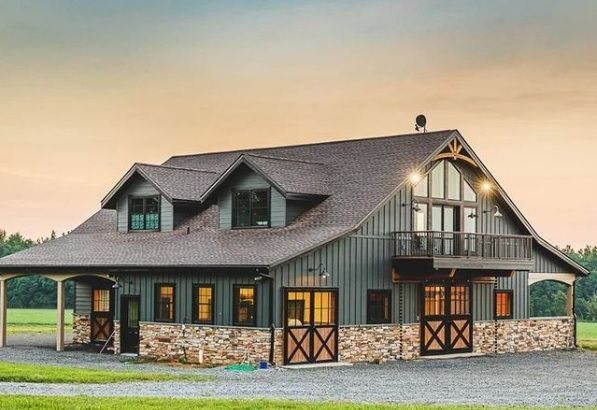 Barn-style house with a stone base, dark grey siding, and a brown roof. Features a porch, balcony, and large windows.