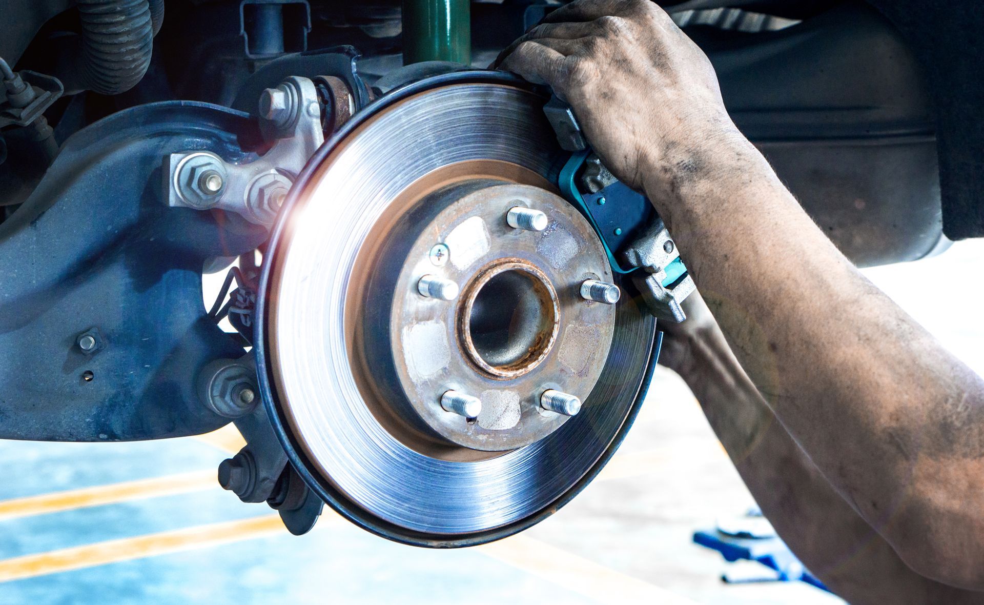 A person is holding two brake pads in their hands in front of a car| Parker's Tire & Auto Service