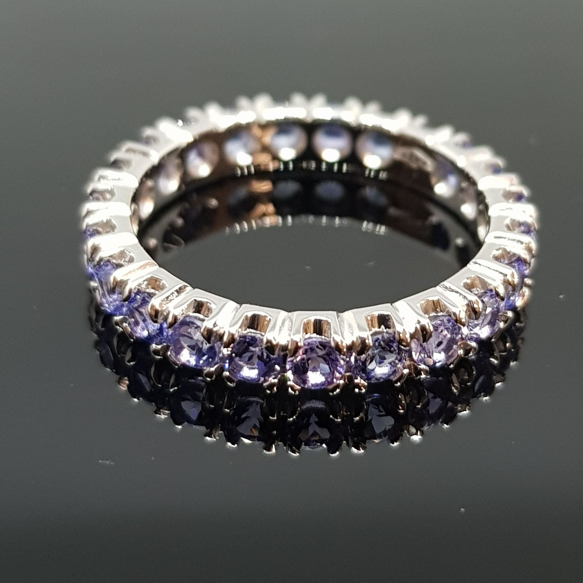 Collana di perline d'argento drappeggiata su una pianta marrone spinosa con una superficie riflettente nera.