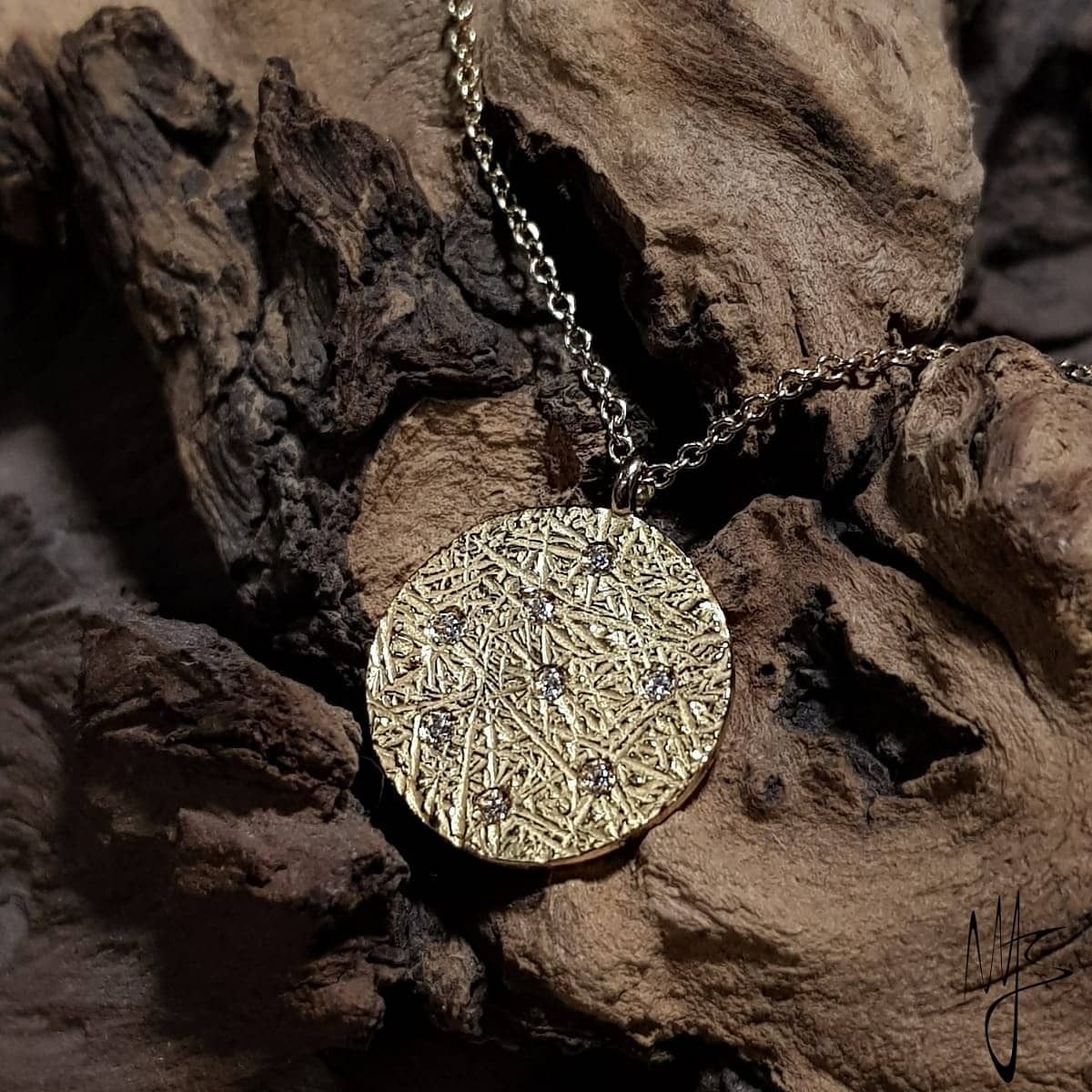 Collana con ciondolo in oro con superficie testurizzata e piccole gemme su sfondo in legno.