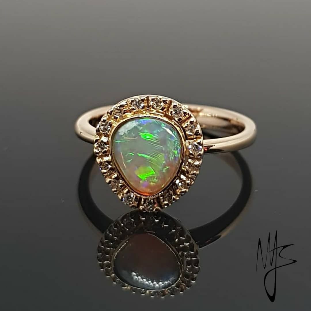 Anello in oro con un opale a forma di pera circondato da piccoli diamanti.