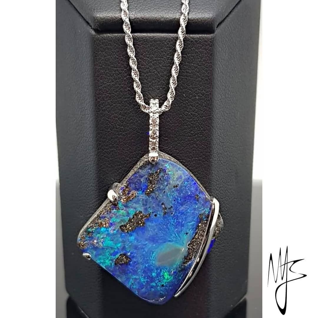 Ciondolo in opale blu con catena in argento, esposto su un supporto nero.