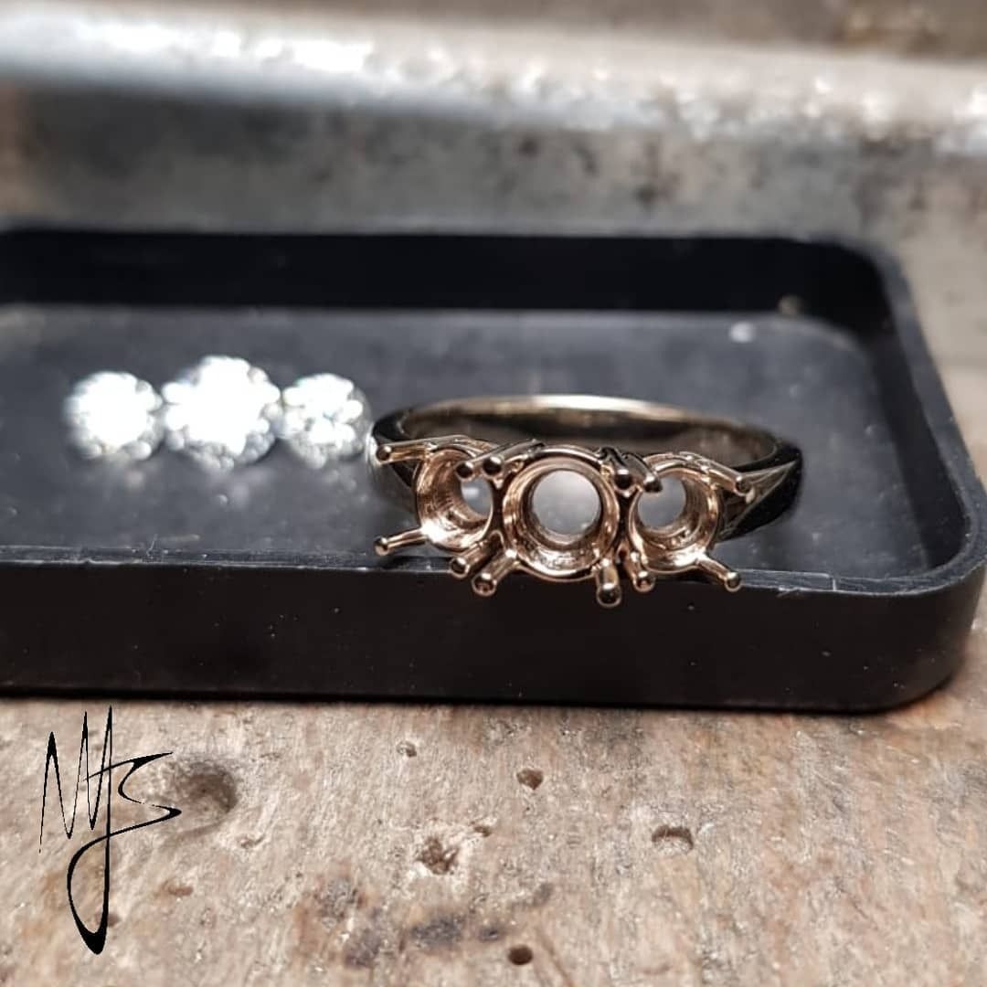 Incastonatura di un anello con tre portapietre vuoti accanto a diamanti sciolti in un vassoio da gioielliere.