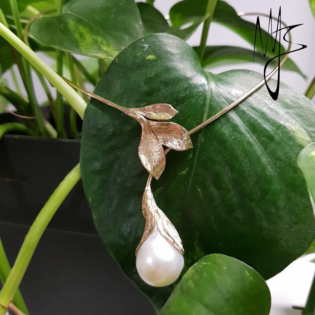 Collana in oro con motivo a foglia e pendente a forma di perla a goccia su una foglia verde.