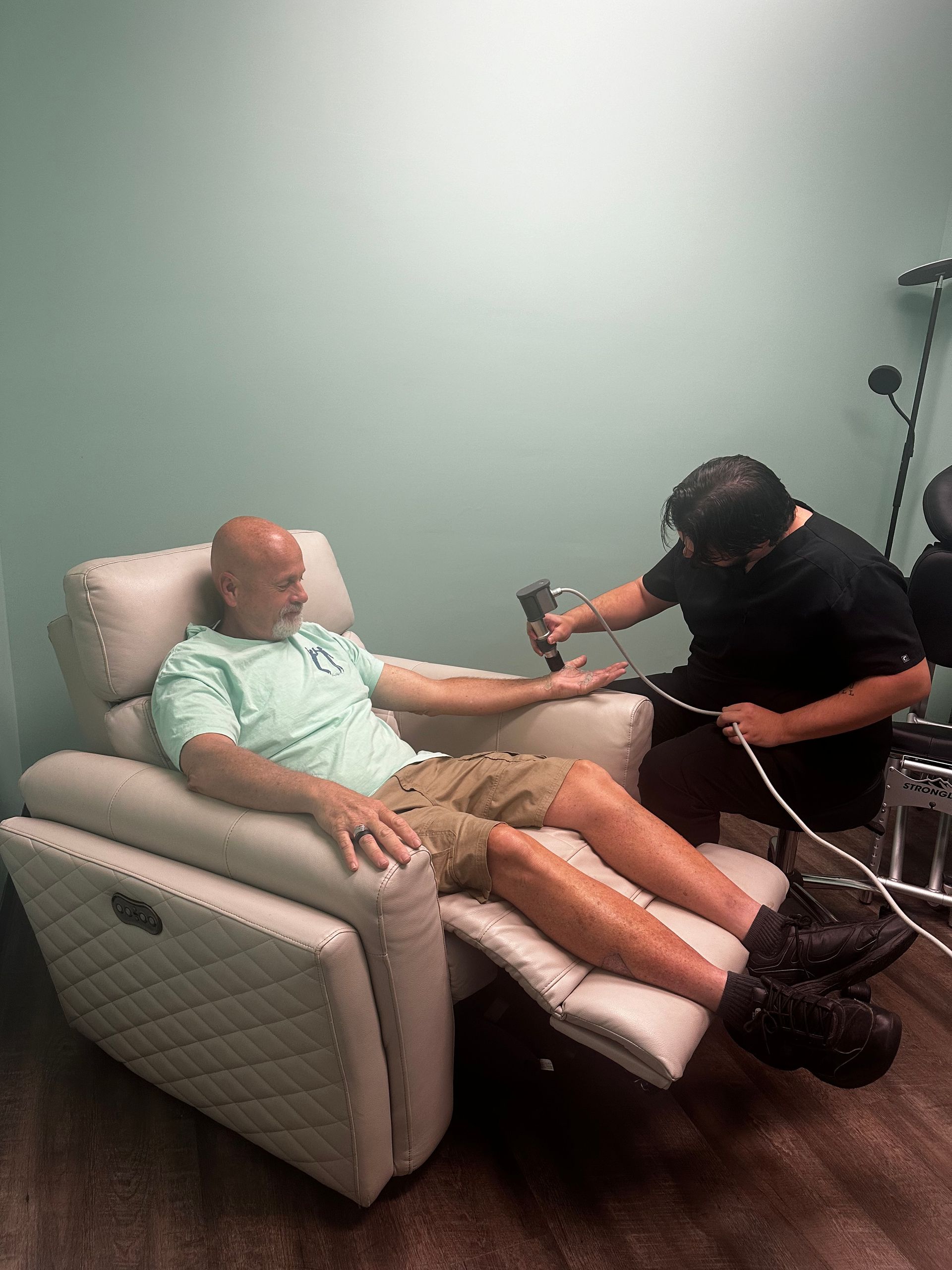 A man is sitting in a chair while a woman holds a hose over his arm.