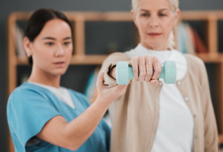 A nurse is helping an elderly woman lift a dumbbell.