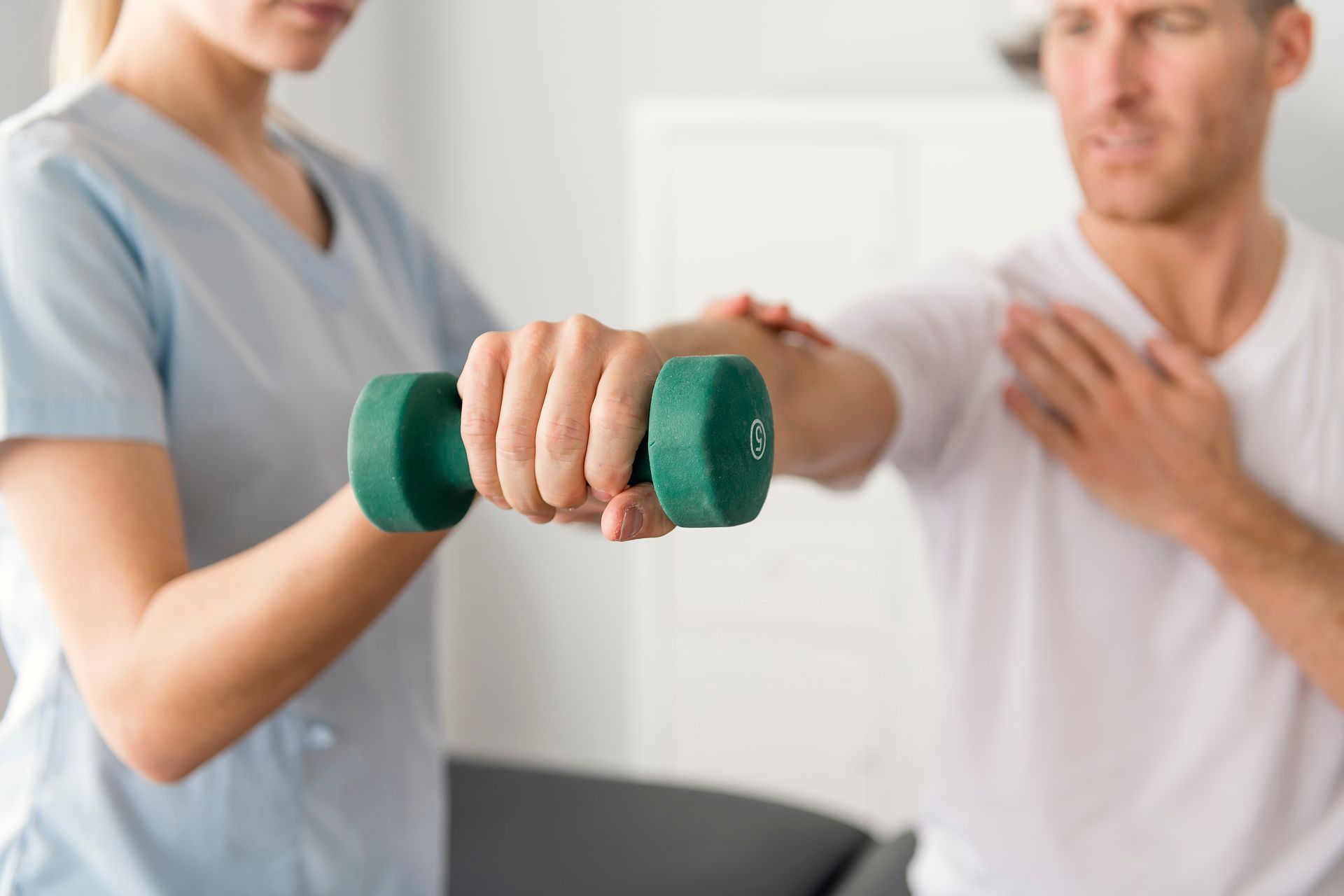 A woman is helping a man lift a green dumbbell.