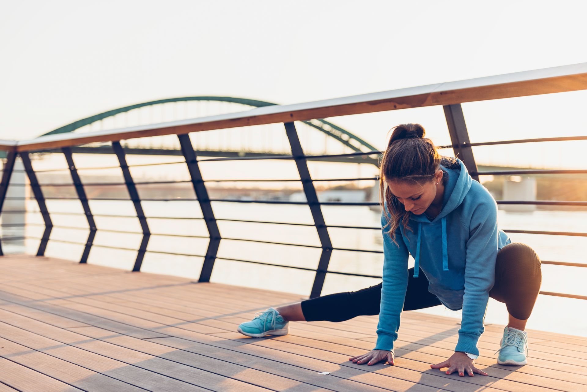 A woman is stretching her legs on a bridge.