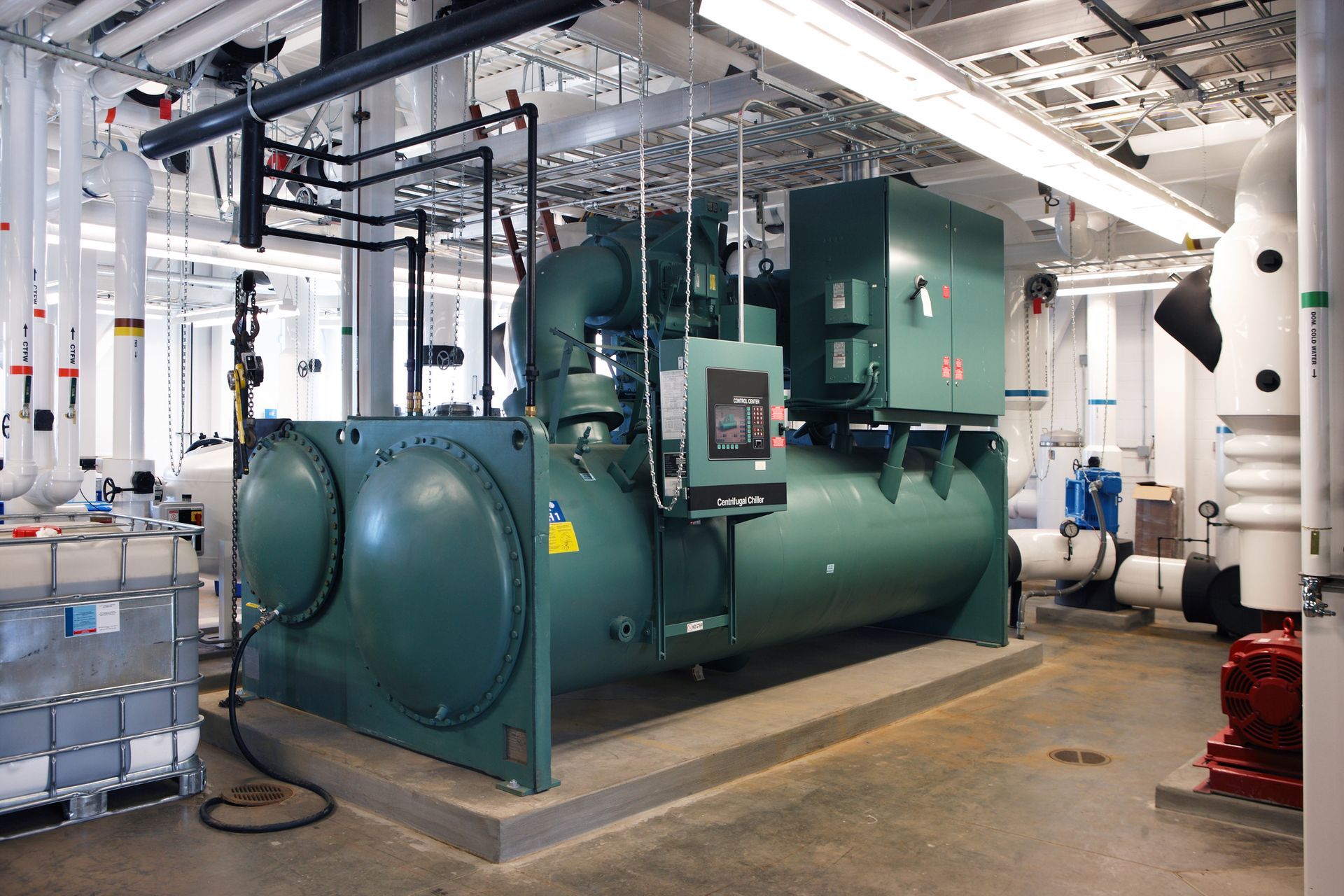Large green chiller unit in a mechanical room with pipes and electrical components.