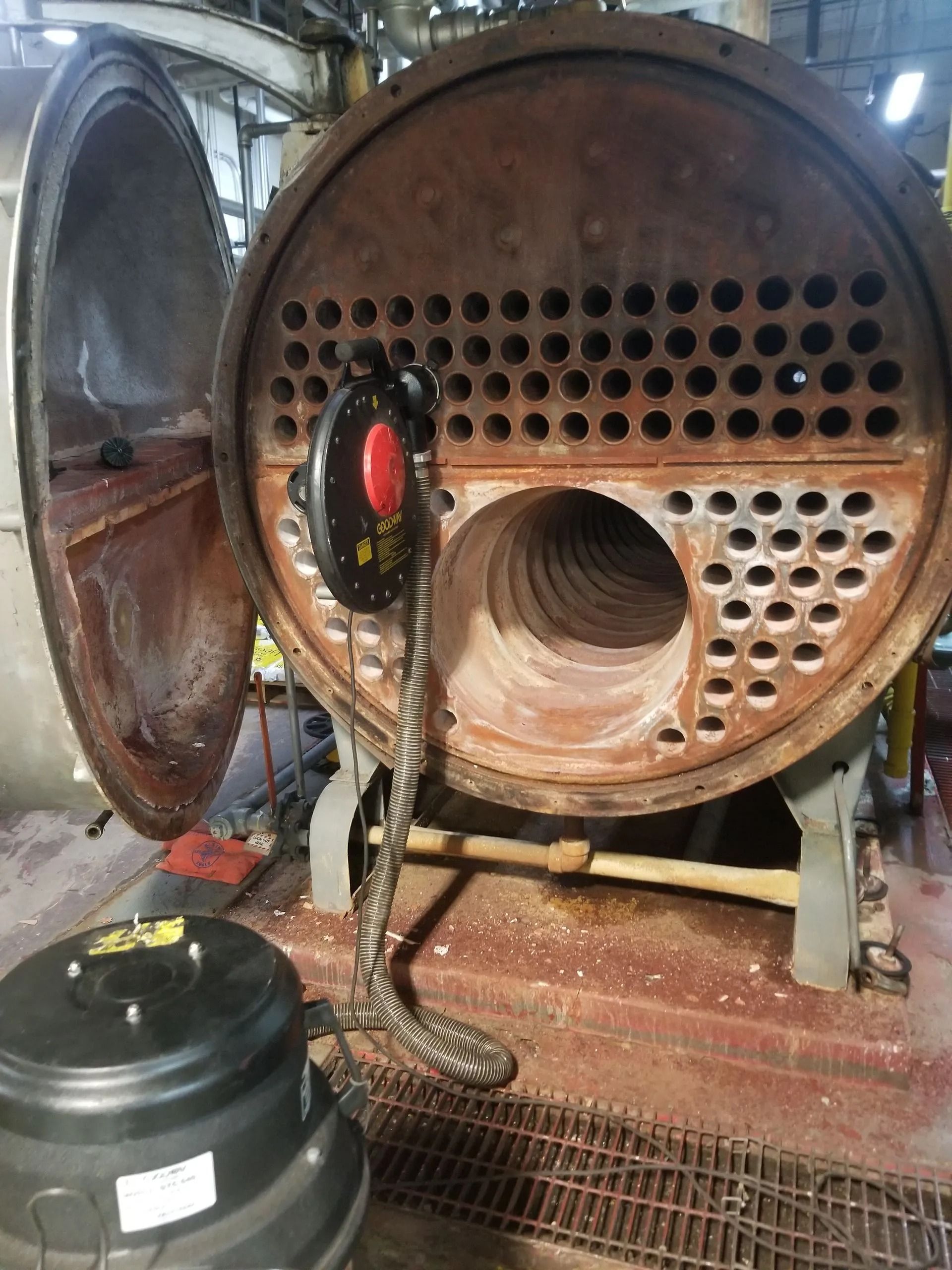 Industrial boiler interior with open access door; black and red device inside.