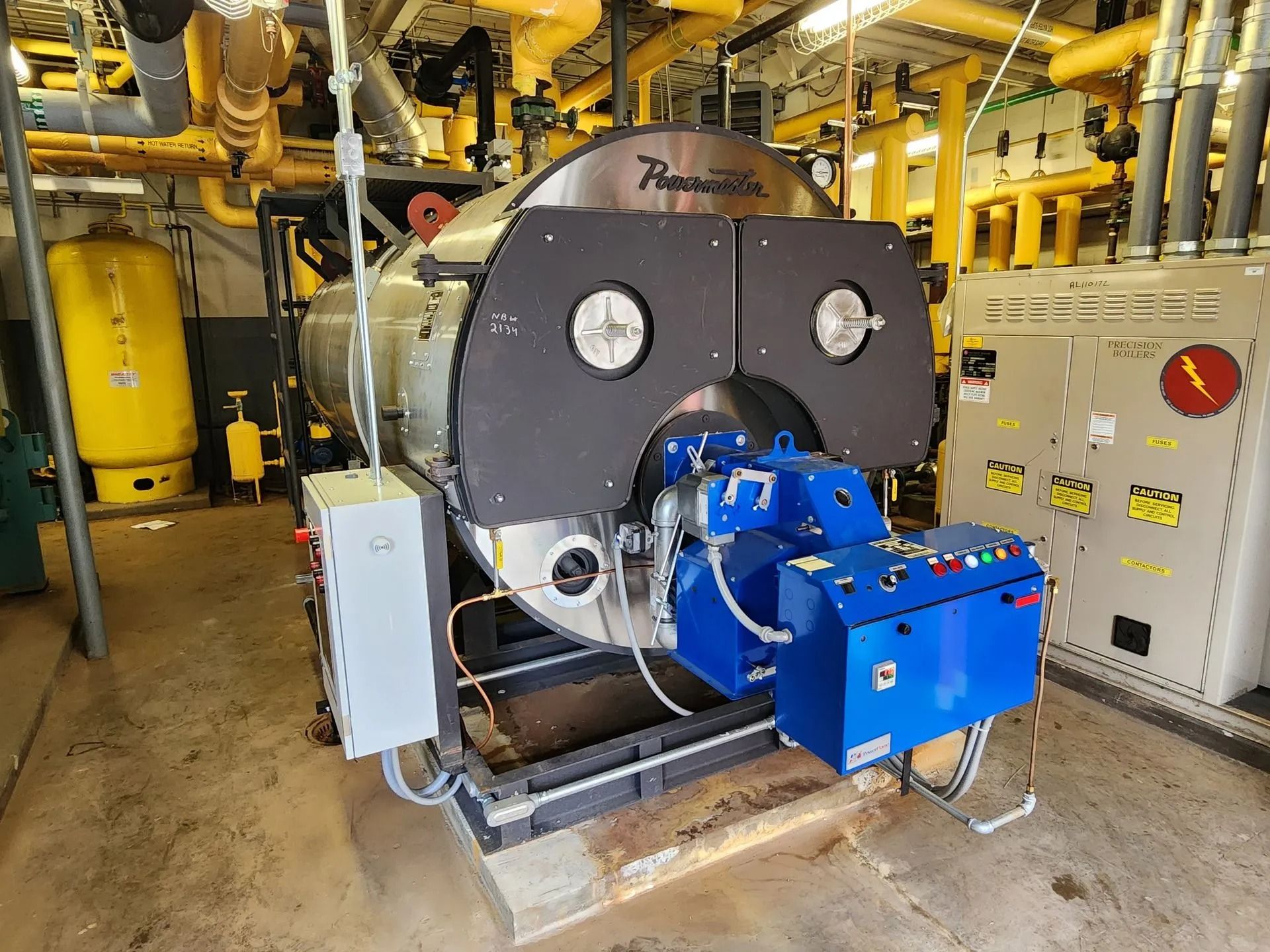 Industrial boiler with blue controls and black front panel in a utility room.