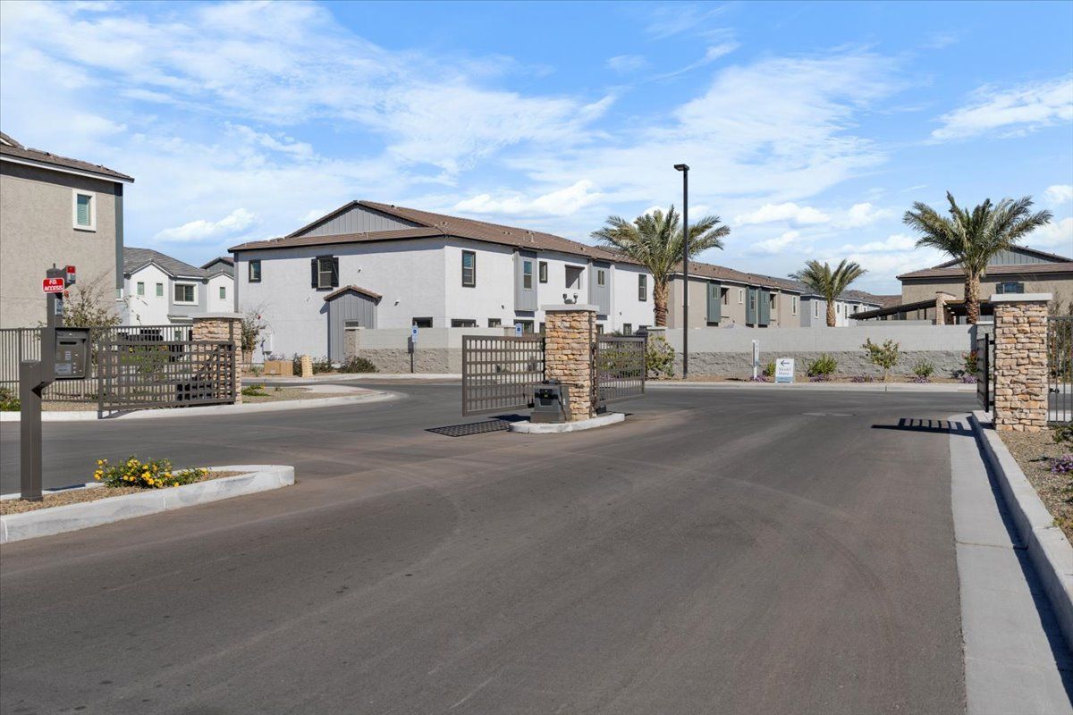 A gated entrance to a residential area with houses and palm trees.