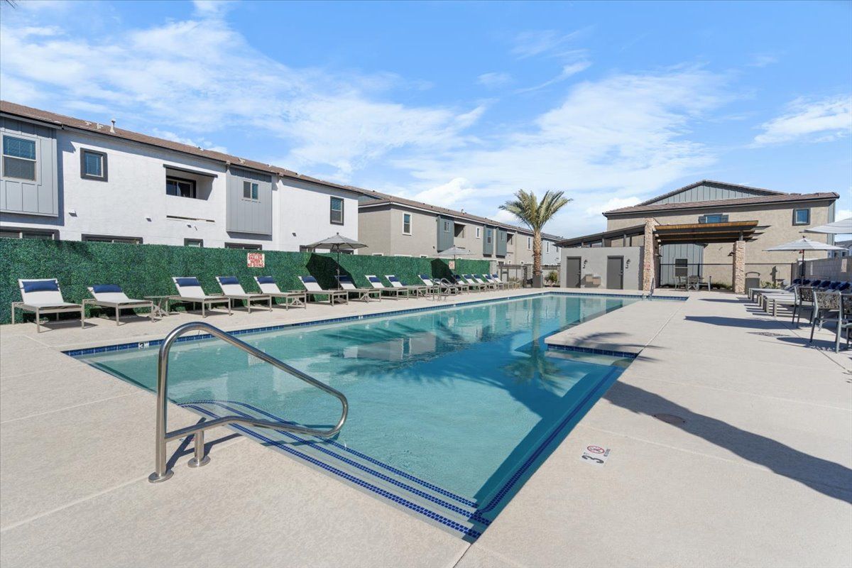A large swimming pool surrounded by chairs and umbrellas in front of a building.