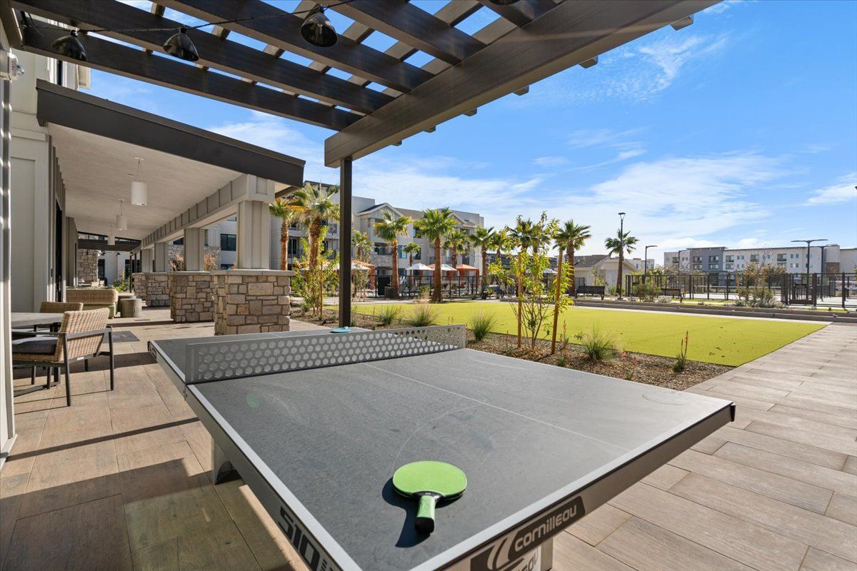 A ping pong table with a green paddle on it under a pergola.
