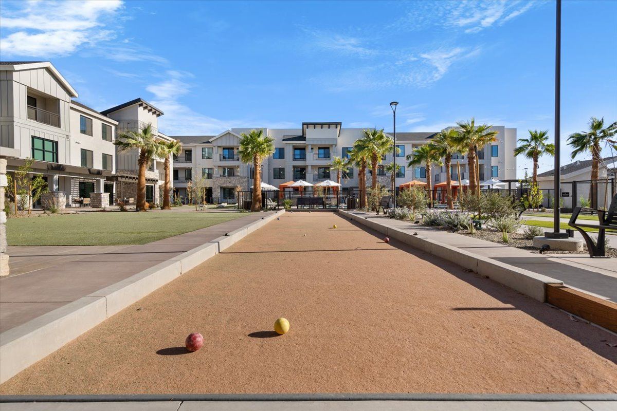 A bocce ball court in front of a large building with palm trees.