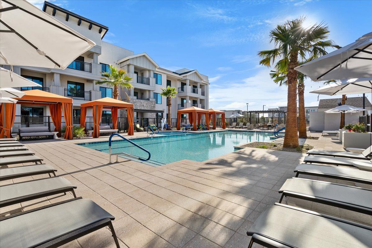 A large swimming pool surrounded by chairs and umbrellas in front of a building.