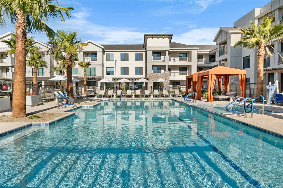A large swimming pool surrounded by palm trees in front of a building.