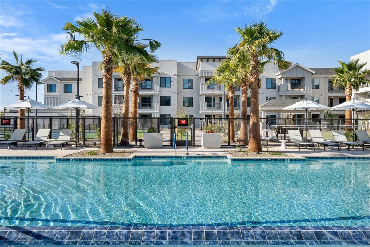 A large swimming pool surrounded by palm trees in front of a building.