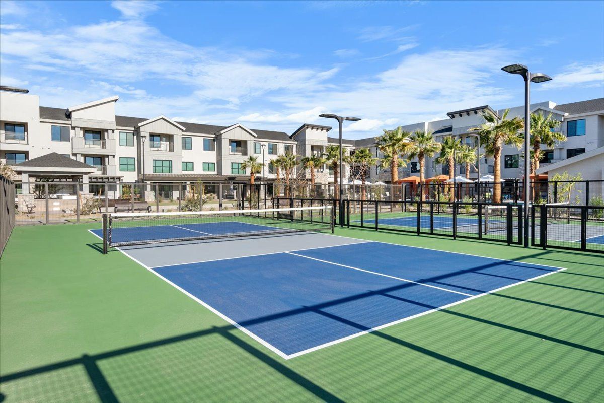 A tennis court in front of a building with palm trees.