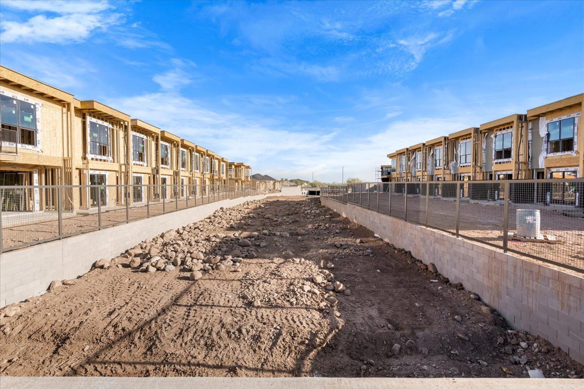 A row of houses under construction with a dirt road leading to them.
