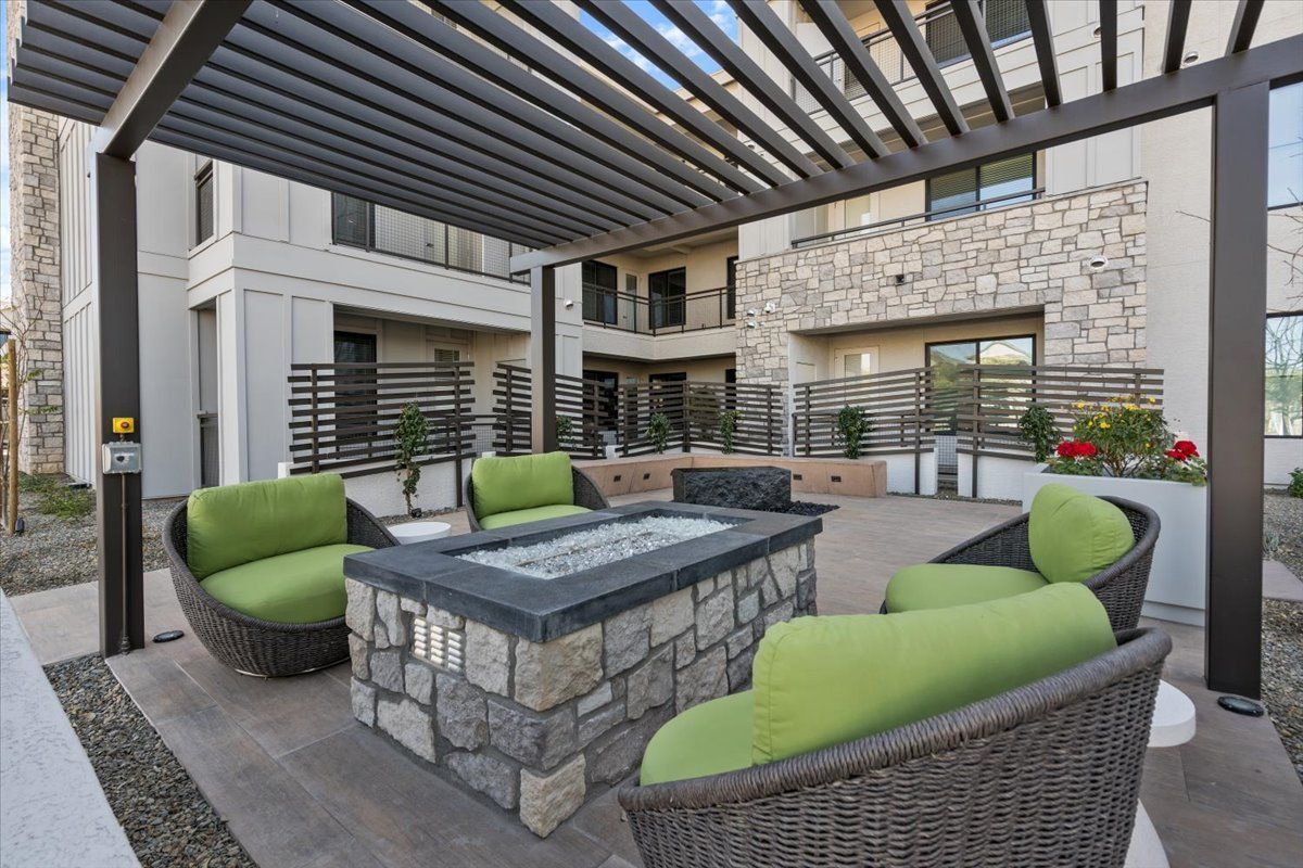 A patio area with a fire pit and chairs under a pergola.