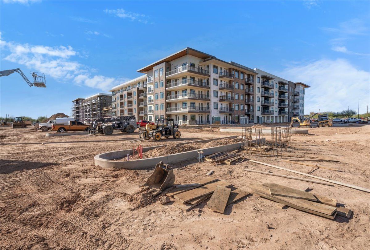 A large building is being built on a dirt field in front of a construction site.