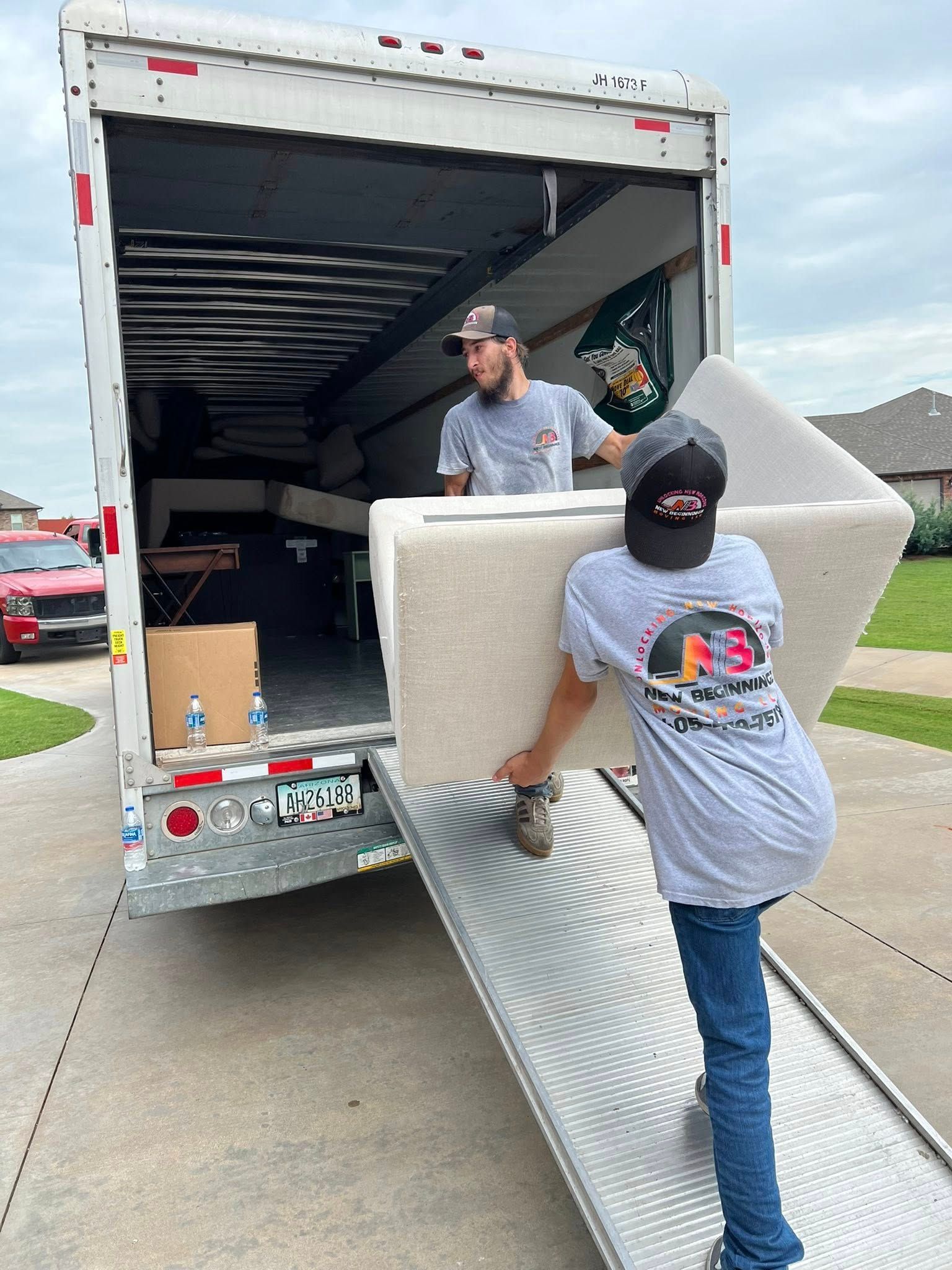 Two men loading a white couch into a moving truck on a driveway.