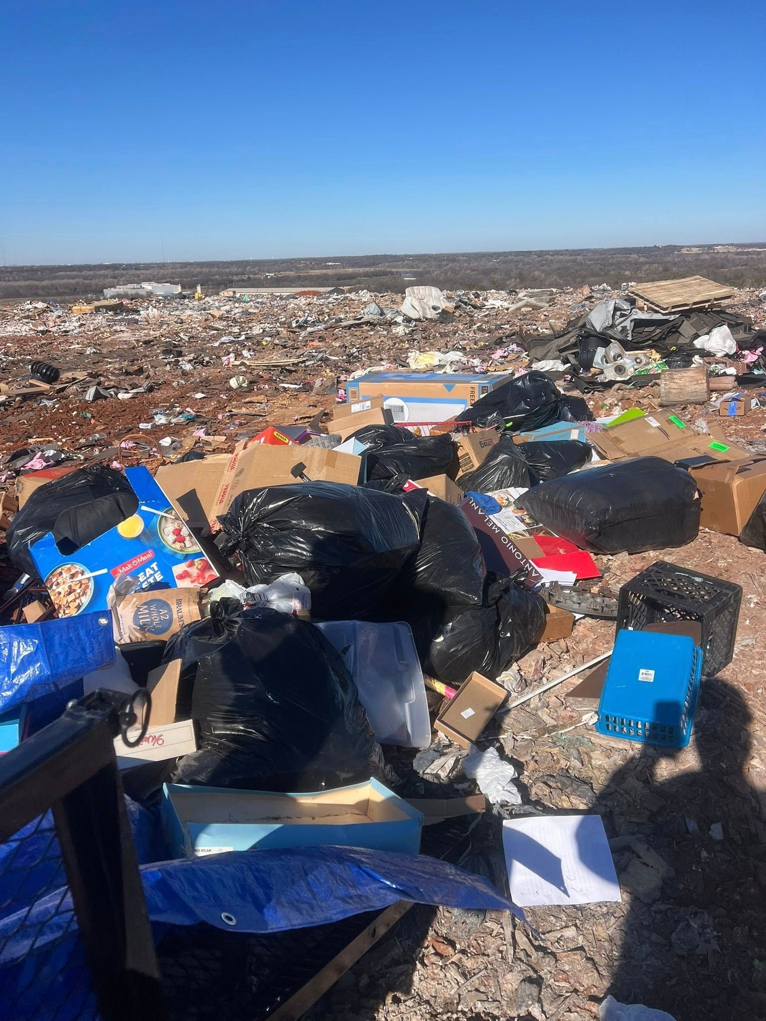 Overflowing landfill with scattered trash and bags under a clear blue sky
