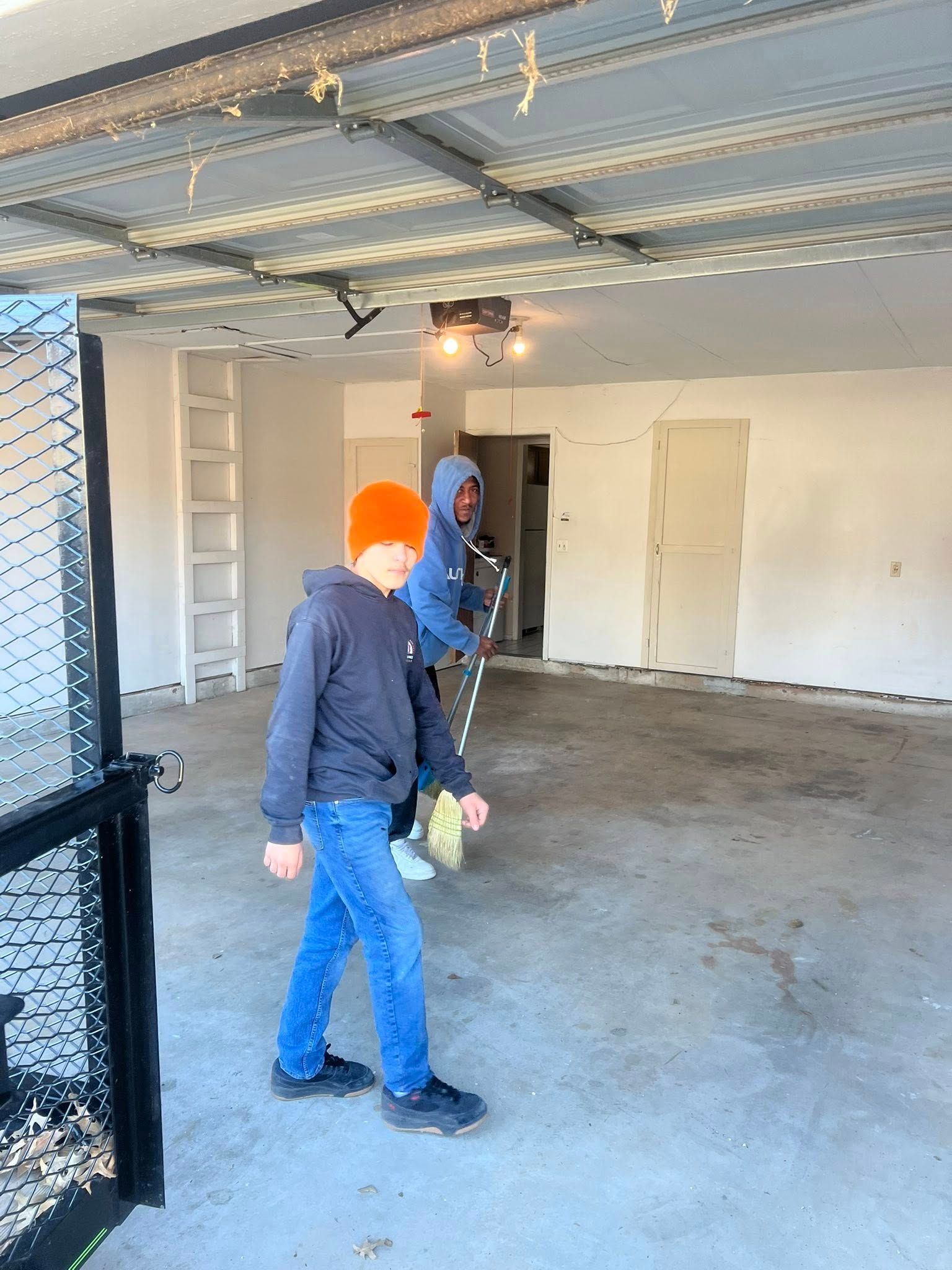 People standing in an unfinished garage with a bare floor, white walls, and a ladder.