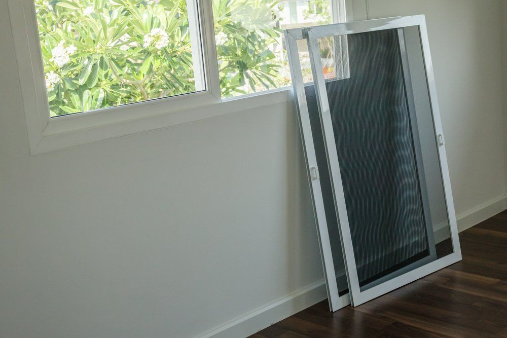Two Grille Screen Doors Are Sitting on a Wooden Floor Next to a Window — Affordable Blinds, Doors & Security Pty Ltd in Tweed Heads South, NSW