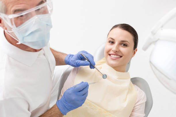 A woman is sitting in a dental chair while a dentist examines her teeth.