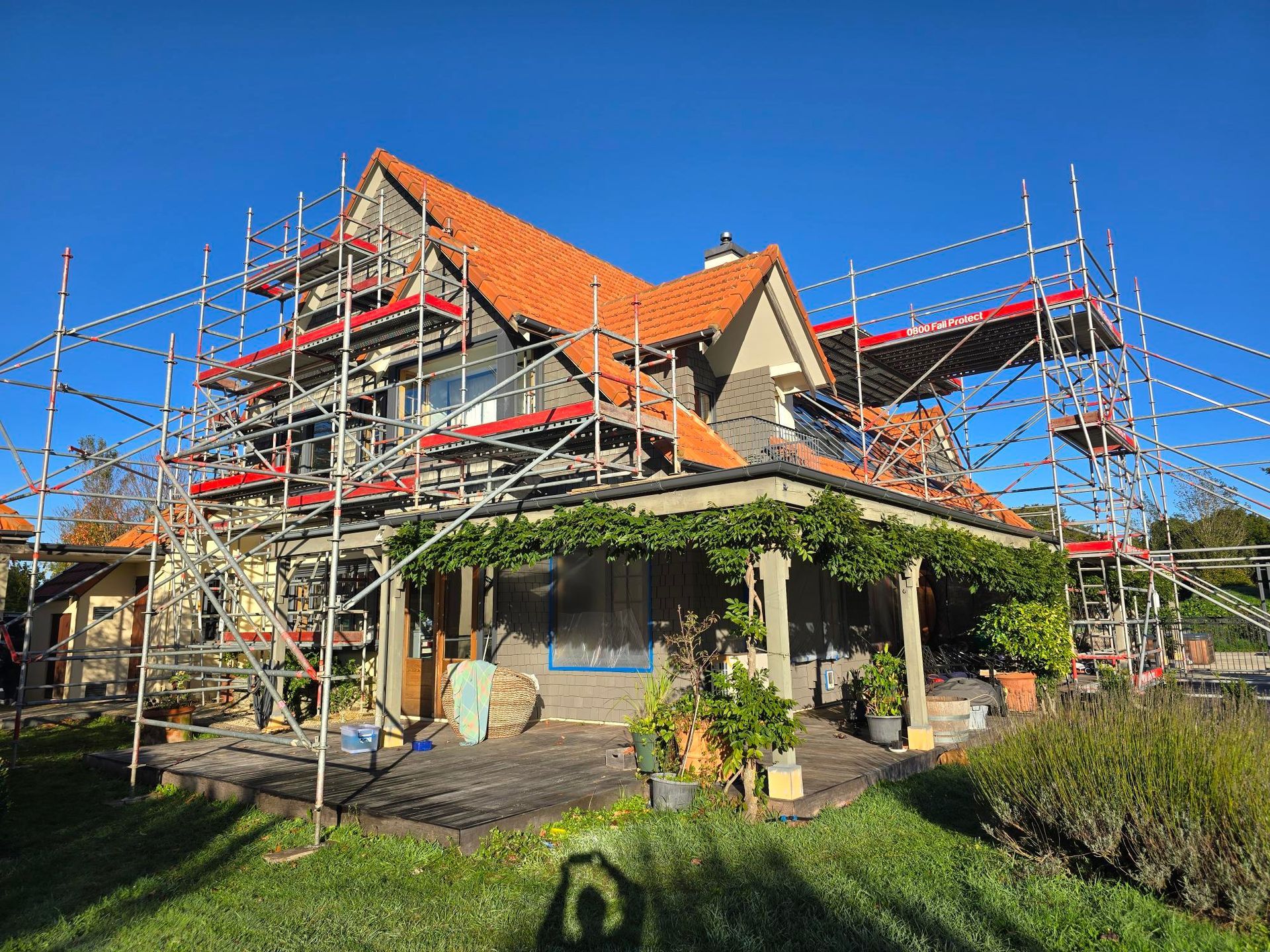 House with scaffolding during renovation, orange roof, green lawn, and clear blue sky.