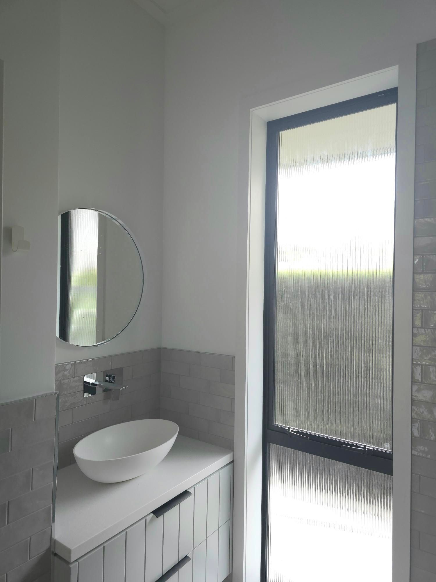 Bathroom with a white sink, mirror, and window. Gray and white tiles.