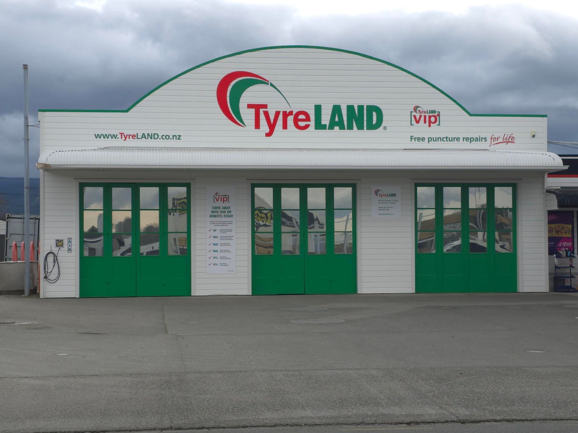 TyreLAND shop with a white facade, green doors, and logo; cloudy sky in background.
